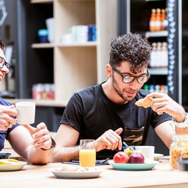 Two young men laughing while having healthy breakfast in a hotel